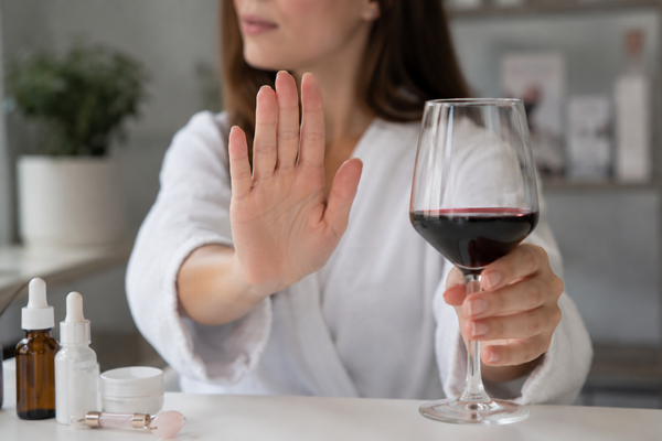 Vrouw houdt een glas rode wijn vast en maakt een afwijzend gebaar na een fillerbehandeling